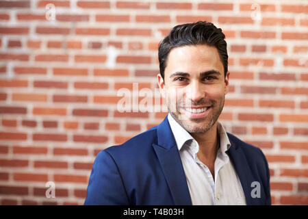Portrait Of Smiling Mature Businessman Standing Against Brick Wall In Modern Office Stock Photo