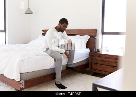 Depressed Man Looking Unhappy Sitting On Side Of Bed At Home Stock Photo