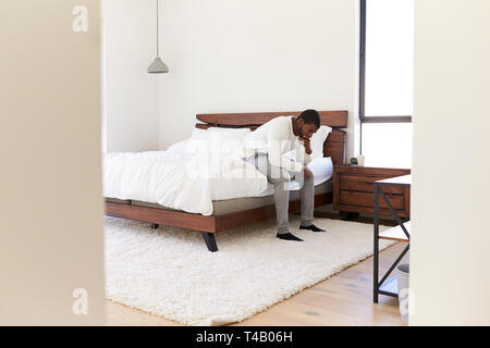 Depressed Man Looking Unhappy Sitting On Side Of Bed At Home Stock Photo