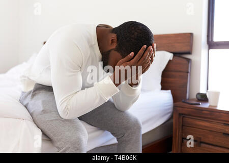 Depressed Man Looking Unhappy Sitting On Side Of Bed At Home With Head In Hands Stock Photo