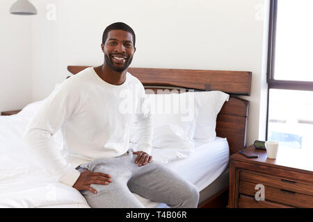 Portrait Of Smiling Man Sitting On Side Of Bed At Home Looking Positive Stock Photo