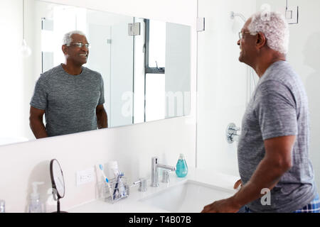 Smiling Senior Man Looking At Reflection In Bathroom Mirror Wearing Pajamas Stock Photo