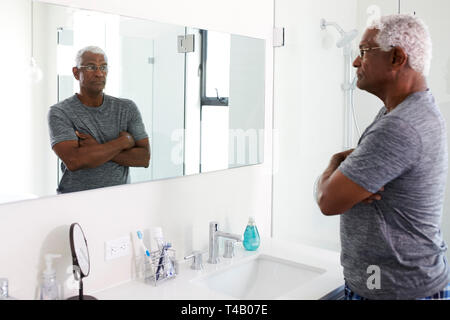 Unhappy Depressed Senior Man Looking At Reflection In Bathroom Mirror Stock Photo