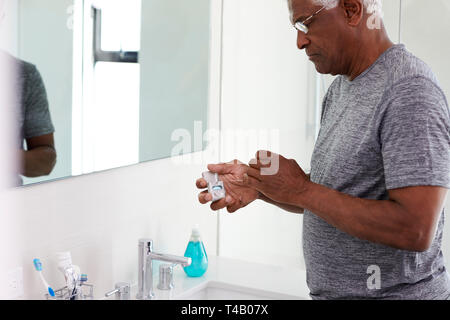 Senior Man Flossing Teeth Standing Next To Bathroom Mirror Wearing Pajamas Stock Photo