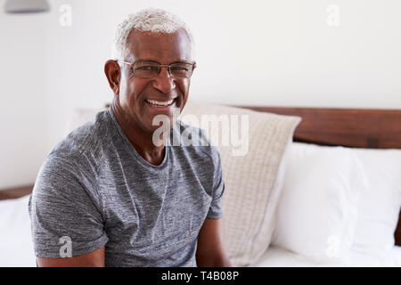 Portrait Of Smiling Senior Man Sitting On Side Of Bed At Home Looking Positive Stock Photo