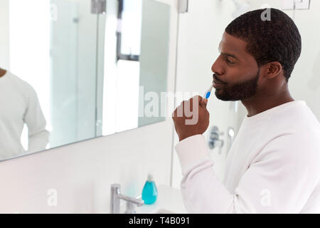 Man Looking At Reflection In Bathroom Mirror Brushing Teeth Stock Photo