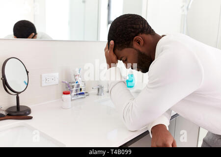 Depressed Man Leaning On Sink In Bathroom With Head In Hands Stock Photo