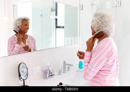 Senior Woman Looking At Reflection In Bathroom Mirror Brushing Hair Stock Photo
