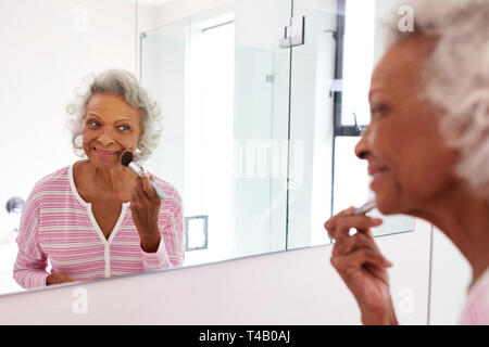 Senior Woman Looking At Reflection In Bathroom Mirror Putting On Make Up Stock Photo