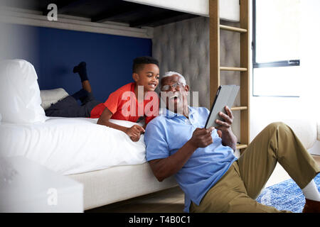 Grandfather With Grandson Lying In Bedroom Playing Game On Digital Tablet Together Stock Photo