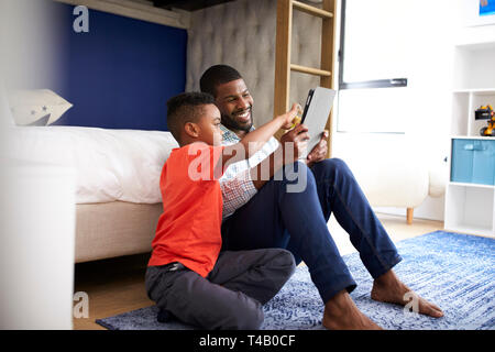 Father With Son Sitting In Bedroom Playing Game On Digital Tablet Together Stock Photo