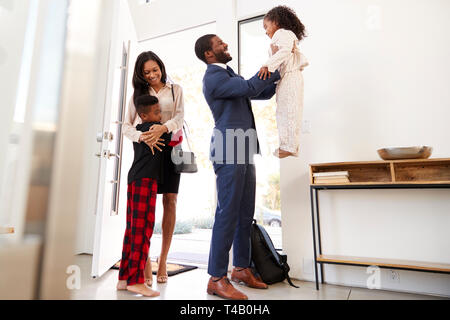 Children Greeting And Hugging Working Parents As They Return Home From Work Stock Photo