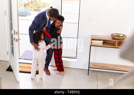 Children Greeting And Hugging Working Businessman Father As He Returns Home From Work Stock Photo