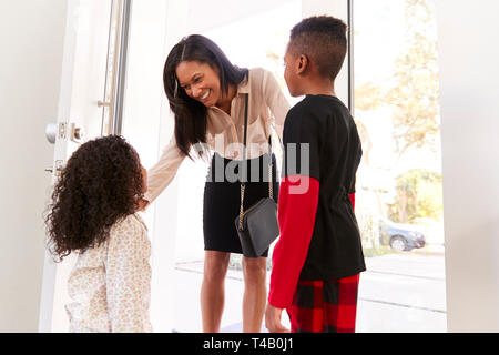 Children Greeting And Hugging Working Businesswoman Mother As She Returns Home From Work Stock Photo