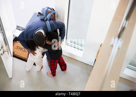 Children Greeting And Hugging Working Businessman Mother As She Returns Home From Work Stock Photo