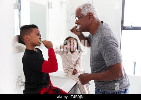 Grandfather In Bathroom Wearing Pajamas Brushing Teeth With Grandchildren Stock Photo