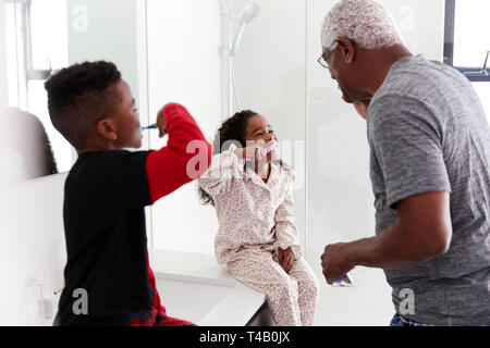 Grandfather In Bathroom Wearing Pajamas Brushing Teeth With Grandchildren Stock Photo