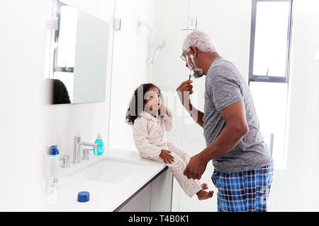 Grandfather Wearing Pajamas In Bathroom Shaving Whilst Granddaughter Watches Stock Photo