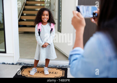 Mother Taking Photo Of Daughter With Cell Phone On First Day Back At School Stock Photo