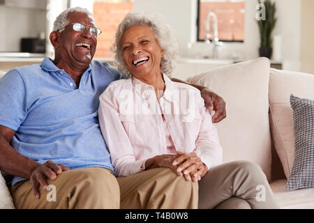 Loving Senior Couple Sitting On Sofa At Home And Laughing Together Stock Photo