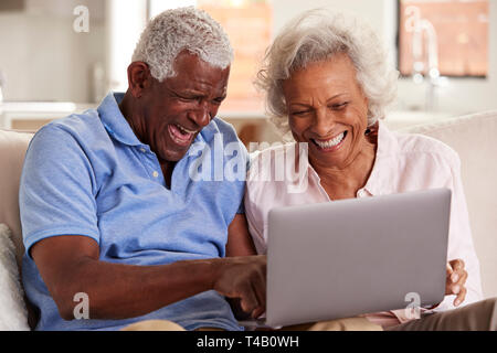 Senior Couple Sitting On Sofa At Home Together Using Laptop Stock Photo