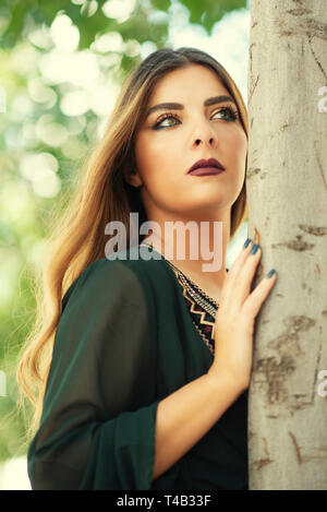 Beautiful young woman leaning against tree looking away Stock Photo