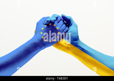 Unification of forces. Two male hands colored in flag of European Unity and Ukraine isolated on grey studio background. Concept of help, partnership of countries, political and economical relations. Stock Photo
