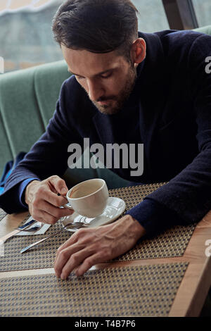 Thinking handsome bearded man sitting in cafe and drinking cup of coffee on the breakfast. Closeup toned portrait Stock Photo