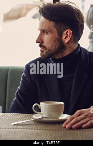 Thinking handsome man sitting in cafe and drinking cup of coffee on the breakfast. Closeup toned portrait. Profile view Stock Photo