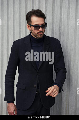 Fashion beard style business handsome male model in fashion sunglasses with serious concentrated look posing in style clothing on wall outdoors backgr Stock Photo