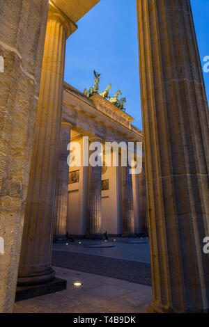 Famous illuminated neoclassical Brandenburg Gate (Brandenburger Tor) in Berlin, Germany, at dusk, viewed between columns. Stock Photo