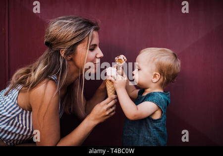 Young mother with small toddler girl outdoors in summer, eating ice cream. Stock Photo