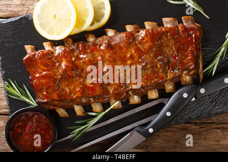 Freshly prepared grilled pork ribs with chili sauce and lemon close-up on a slate board on the table. Horizontal top view from above Stock Photo