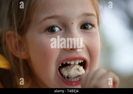 Girl in the campsite, eating porridge, having fun in the outdoors. Active natural lifestyle, family time, home away from home concept. Stock Photo