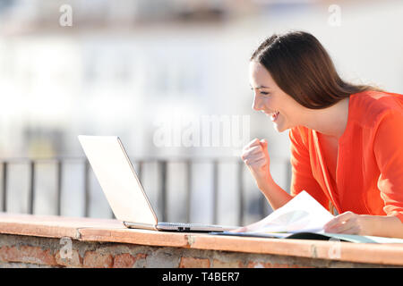Excited self employed checking laptop content outdoors in a balcony Stock Photo