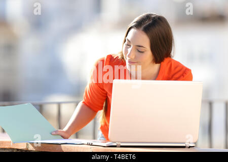 Serious self employed works online with laptop and documents in a balcony Stock Photo