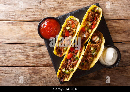 Corn tacos filled with minced beef and vegetables served with sauces close-up on the table. horizontal top view from above Stock Photo