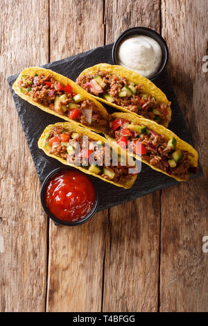 Corn tacos filled with minced beef and vegetables served with sauces close-up on the table. Vertical top view from above Stock Photo