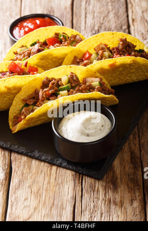 Corn tacos filled with minced beef and vegetables served with sauces close-up on the table. vertical Stock Photo