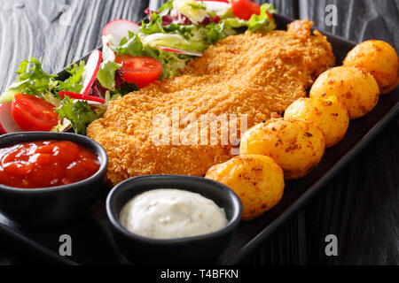 Portion of white fish fillet in breading with new potatoes and fresh vegetable salad close-up on a plate on the table. horizontal Stock Photo