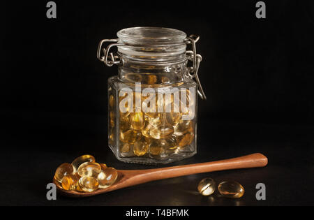 Evening primrose capsules displayed in a jar and on a wooden spoon, against a dark black background Stock Photo