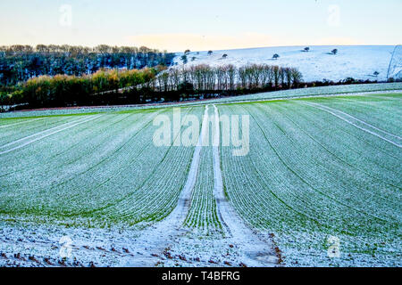 freshly ploughed field covered in a thin layer of white frost forming vertical lines, the field is on a hill and behind is the rolling countryside of  Stock Photo