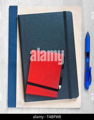 We're Hiring, written on a pile of notebooks, next to a blue pen on a wooden background Stock Photo