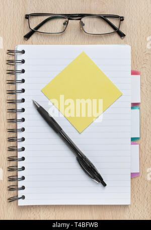 Notebook with blank sticky note on an office or home desk, with glasses and pen Stock Photo