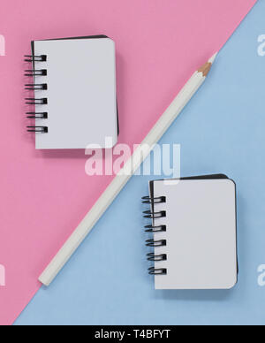 Two open spiral notebooks and a white pencil, on a pink and blue diagonal background. With copy space. Stock Photo