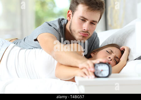 Sleepy couple waking up turning off alarm clock lying in the bed in the morning at home Stock Photo