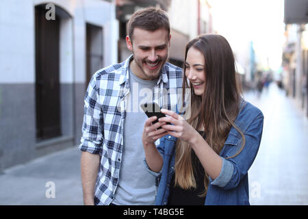 Front view portrait of a happy couple walking using cell phone in the street Stock Photo