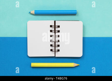 Open spiral notebook with blue and yellow pencils, on a two tone blue background with copy space Stock Photo
