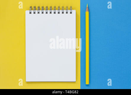 Open blank notepad with a yellow pencil, on a blue and yellow flat lay background. Business/Education concept with copy space. Stock Photo