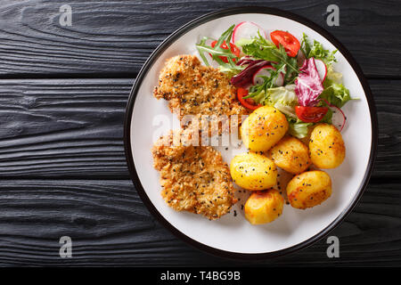 Crispy steaks in sesame breading with new potatoes and fresh salad close-up on a plate on the table. Horizontal top view from above Stock Photo
